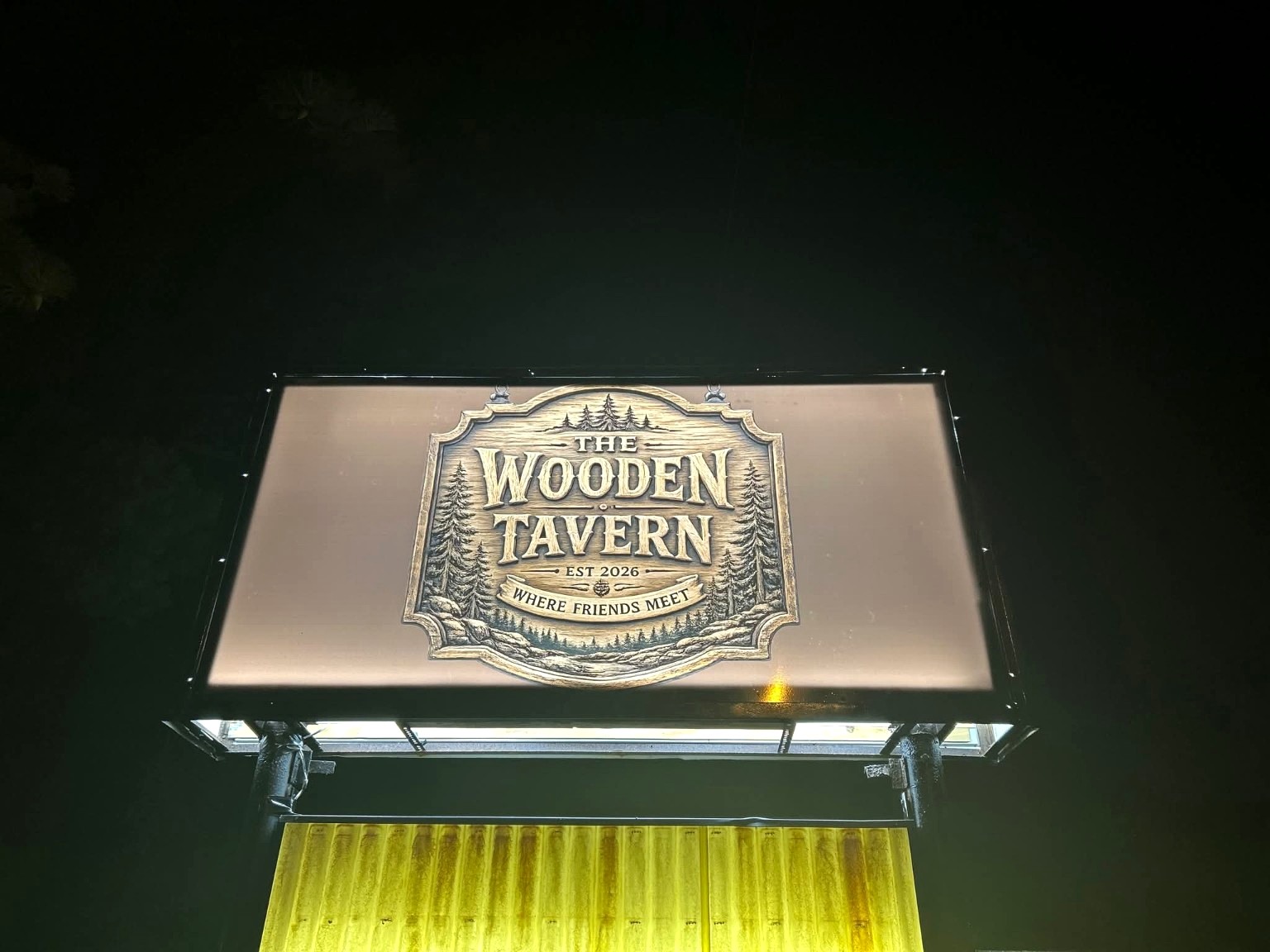 The Wooden Tavern sign lit at night